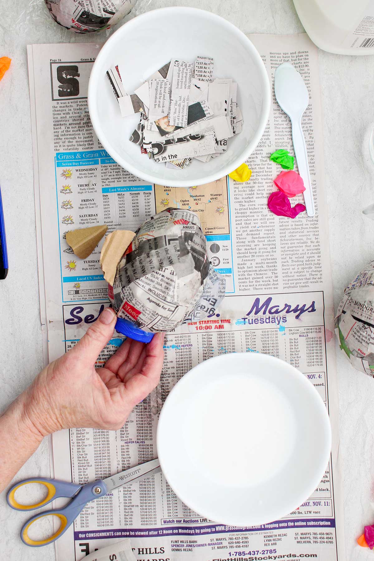 A person securing a blue bottle cap to the bottom of their paper mache project.