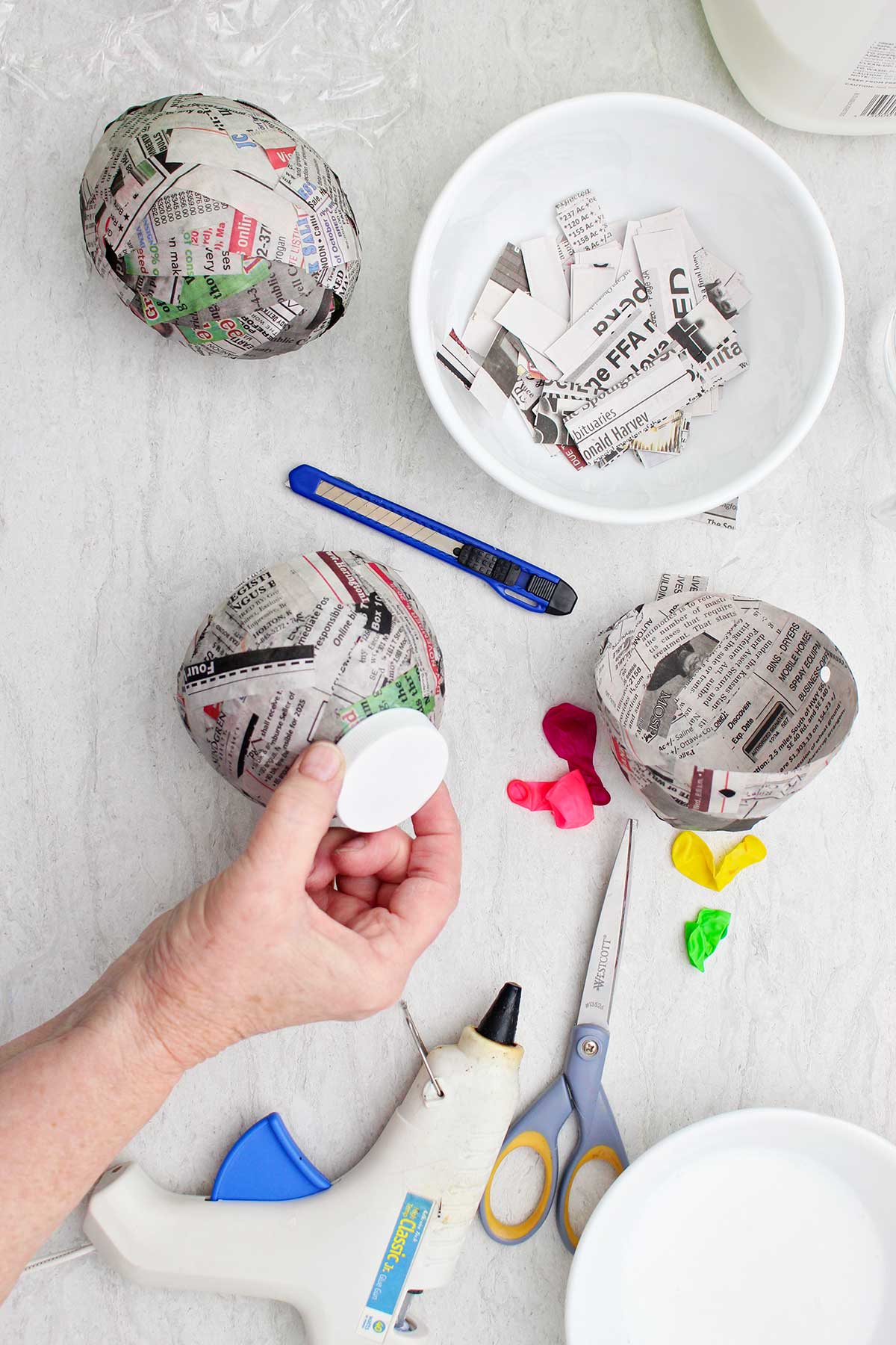 A person securing a white bottle cap to the bottom of their paper mache project.