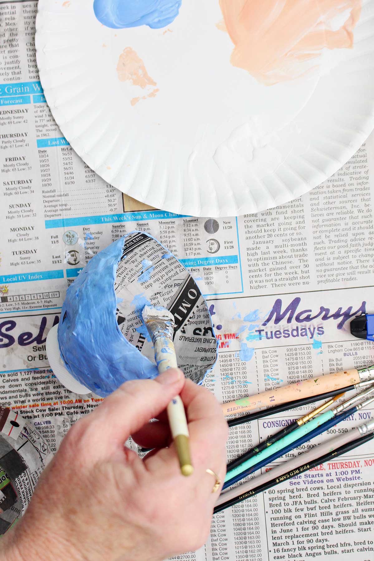 A person painting the inside of their dried paper mache project light blue.