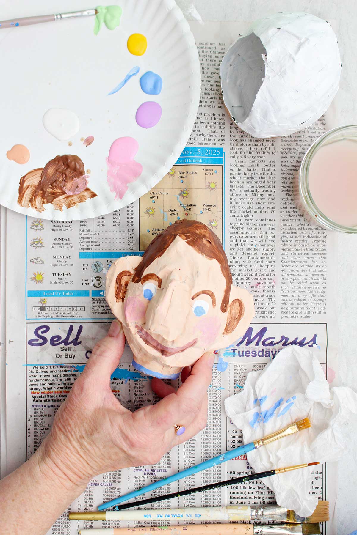 A person holding a painted face made out of paper mache.