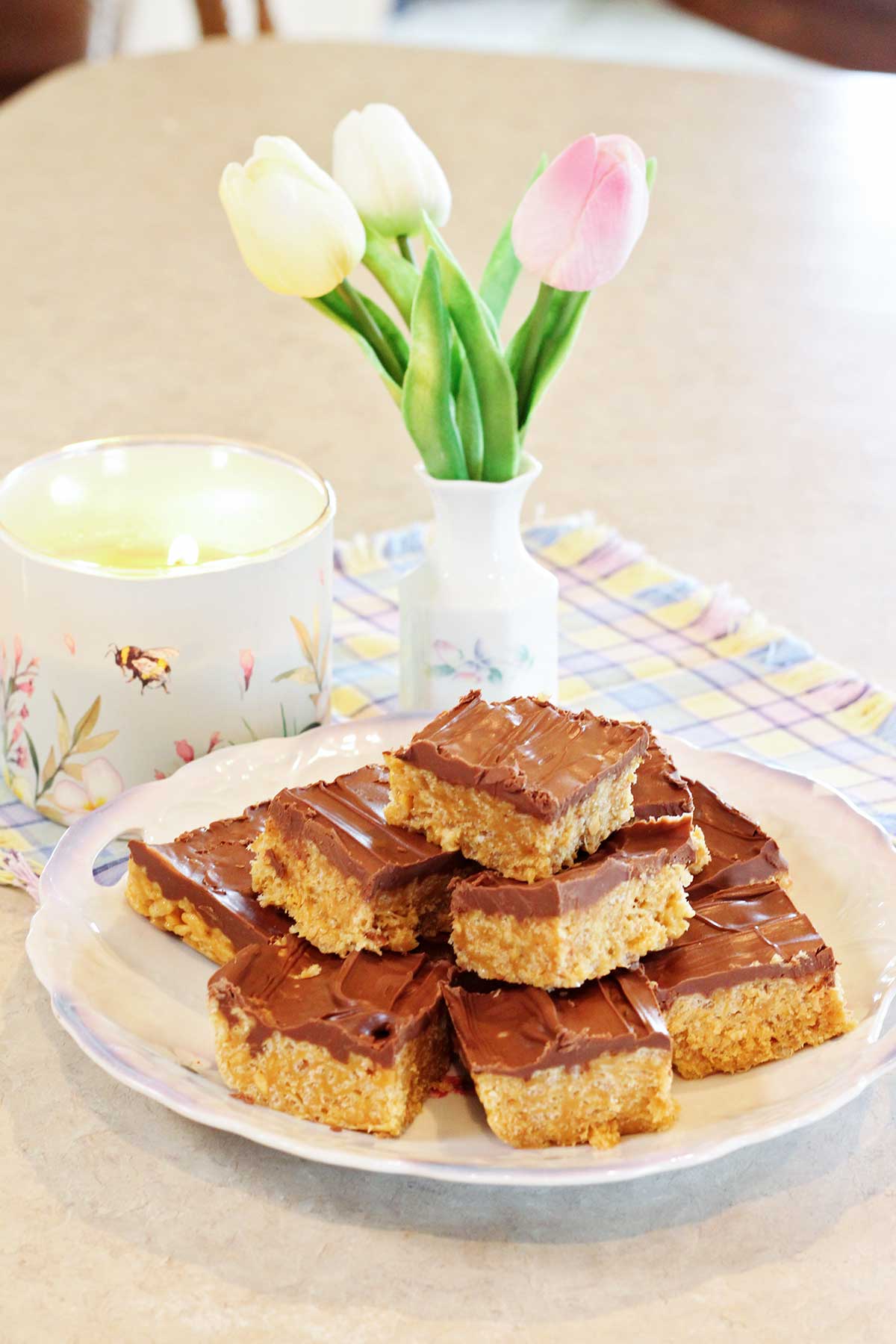 A plate of scotcharoos on a counter near a lit candle and a small vase of tulips.