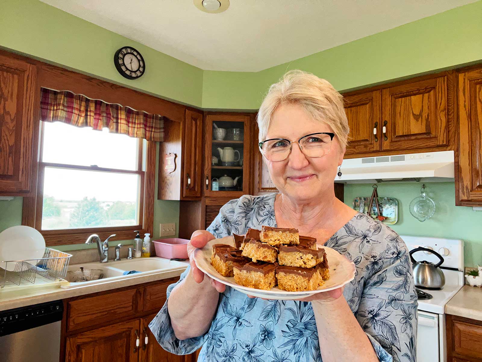 Nana smiling and holding a plate of scotcharoos in her kitchen.