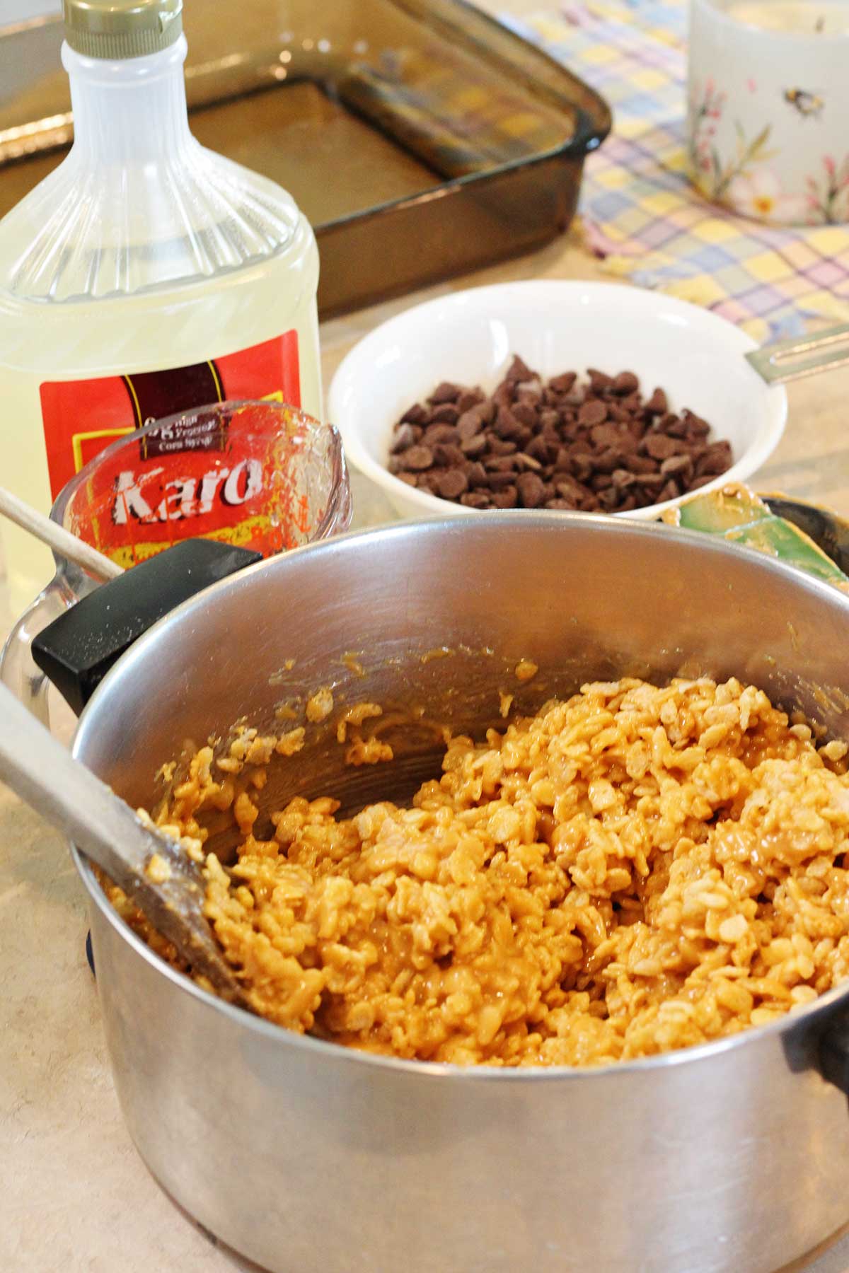 Rice crispy mixture in a pot with chocolate chips and karo syrup near by.
