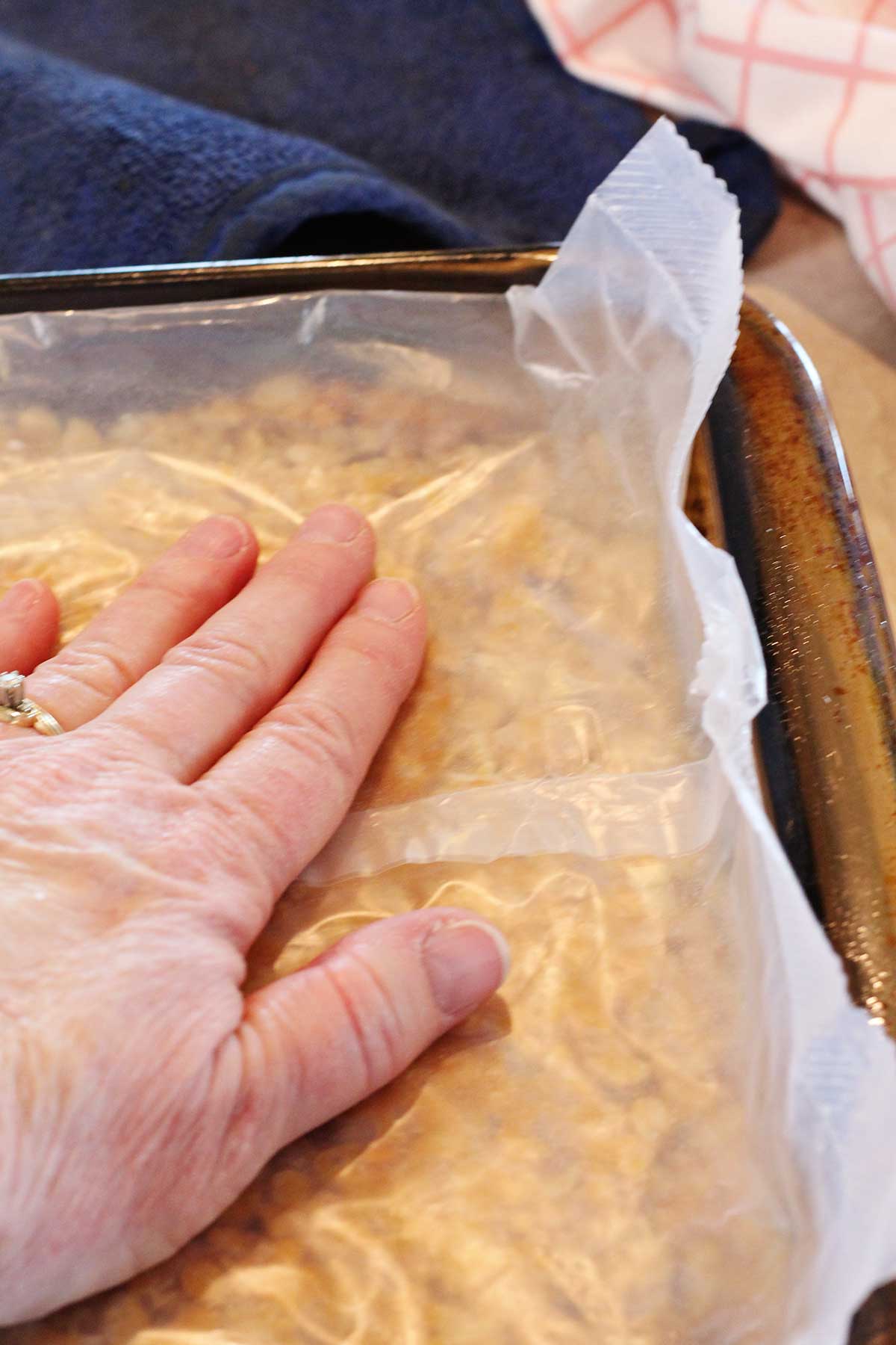 A person pressing the scotcharoos down with a piece of wax paper to avoid sticking.