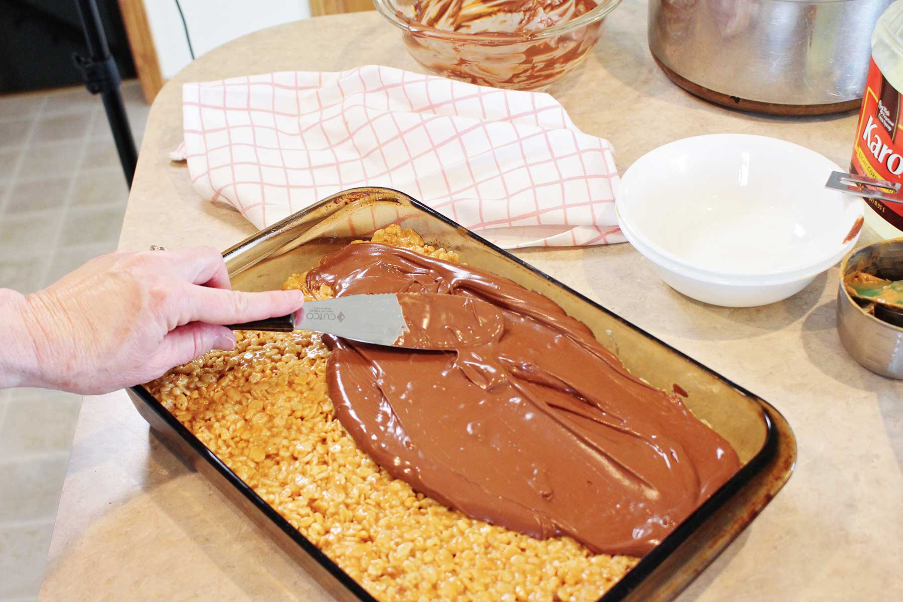 A person using a metal spatula to spread melted chocolate onto scotcharoos.