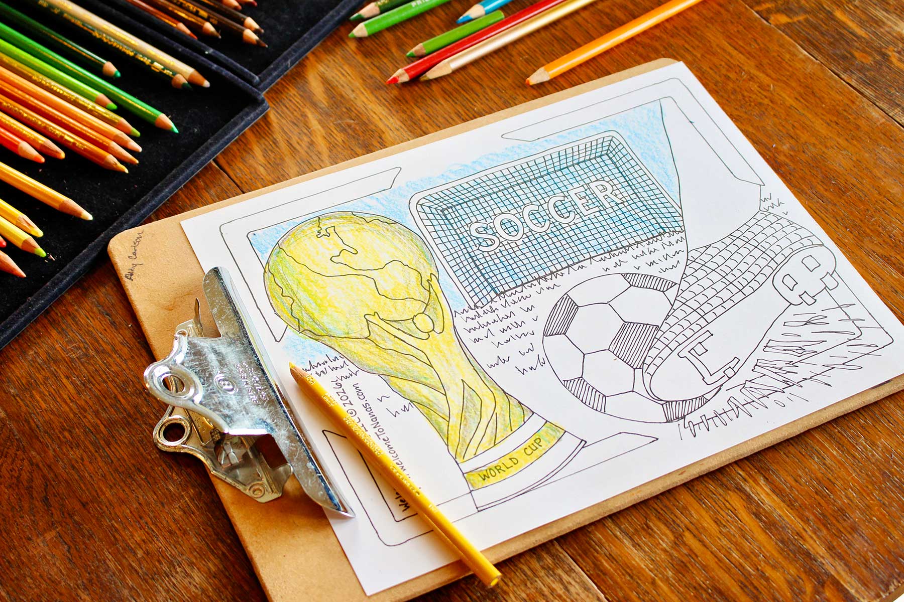 A partially colored in World Cup coloring page coloring sheet featuring a soccer ball being kicked, a soccer goal, and a FIFA World Cup trophy on a wooden table.