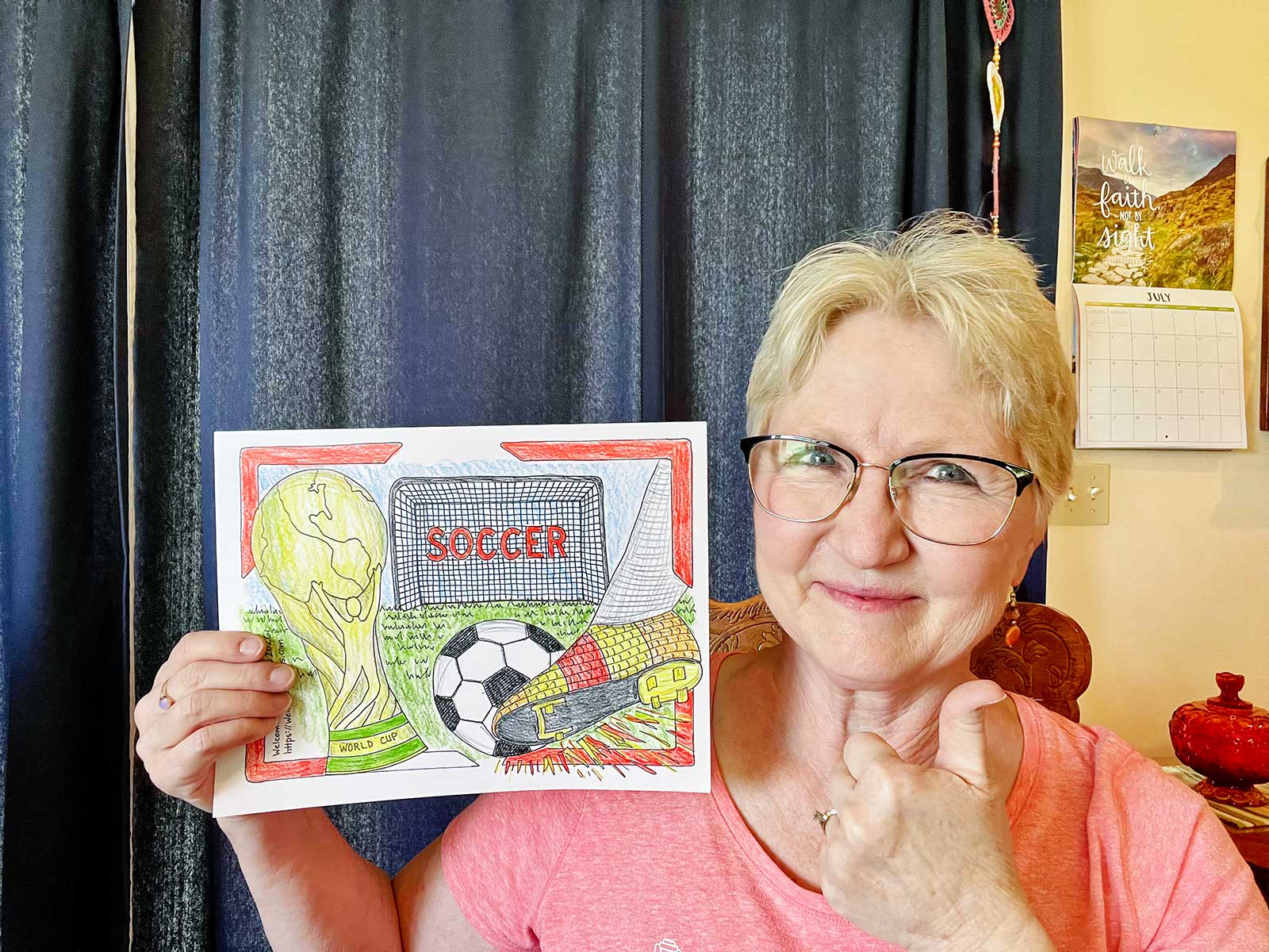 Nana giving a thumbs up in a pink t-shirt holding her fully colored in FIFA World Cup Coloring page.
