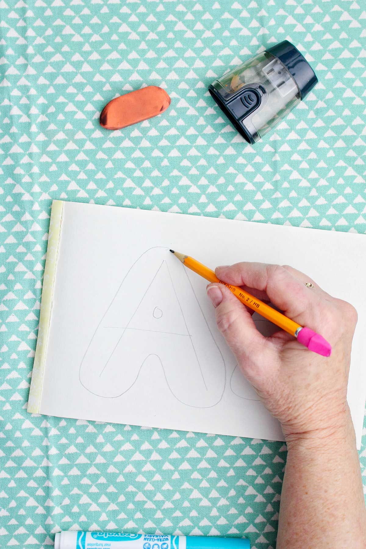 A person sketching a light pencil bubble letter around the pencil drawn "a".