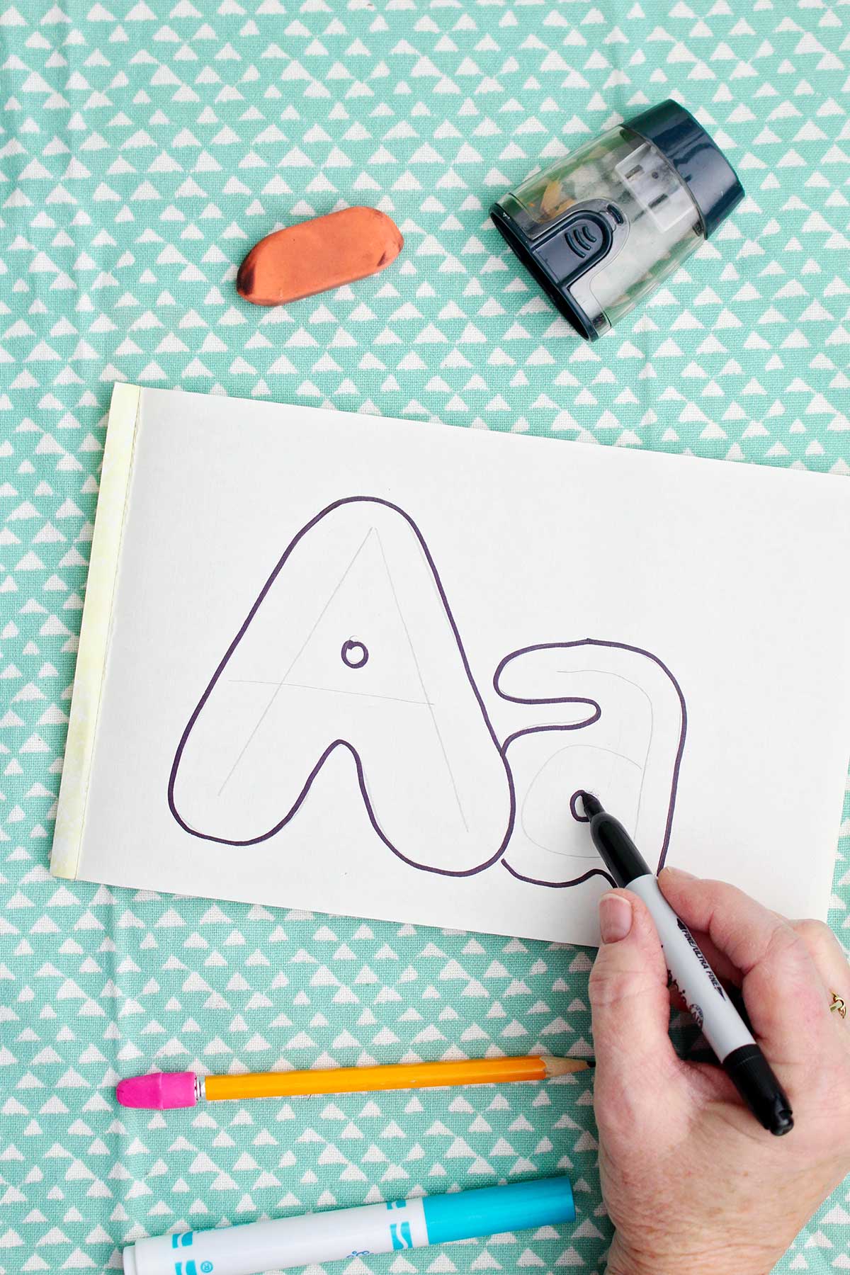 A person outlining with sharpie bubble letters around the pencil drawn "a".