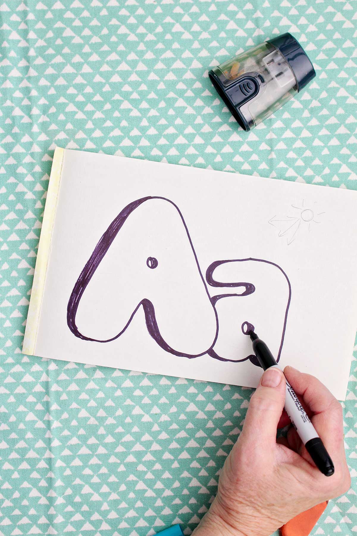 A person using a sharpie marker to add shadow to the upper and lowercase "a".