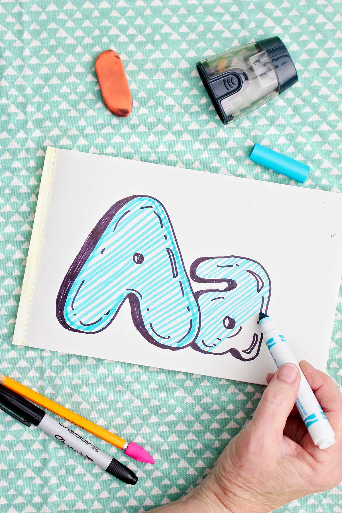 A person using a light blue marker to color in the bubble letters.