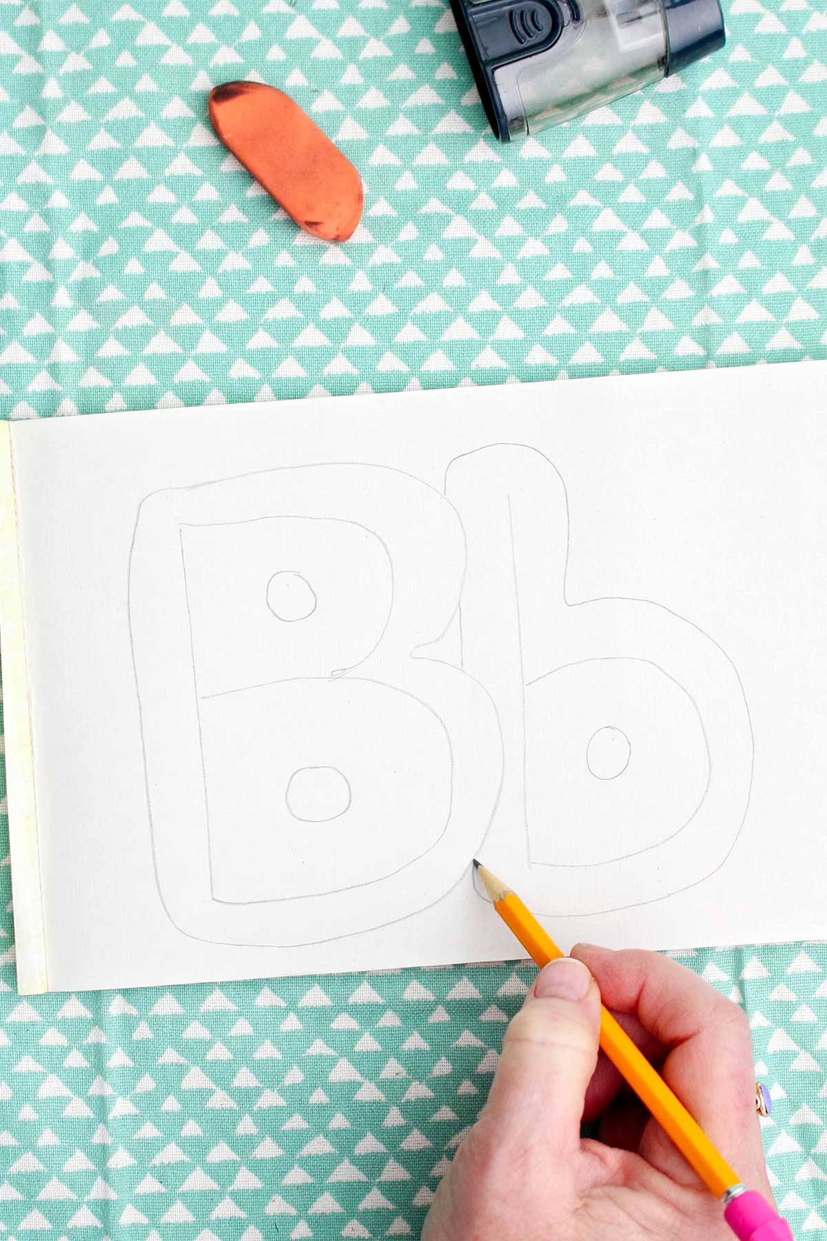 A person sketching a light pencil bubble letter around the pencil drawn "b".