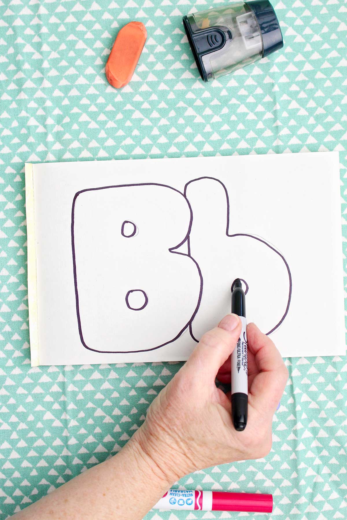 A person outlining with sharpie bubble letters around the pencil drawn "b".