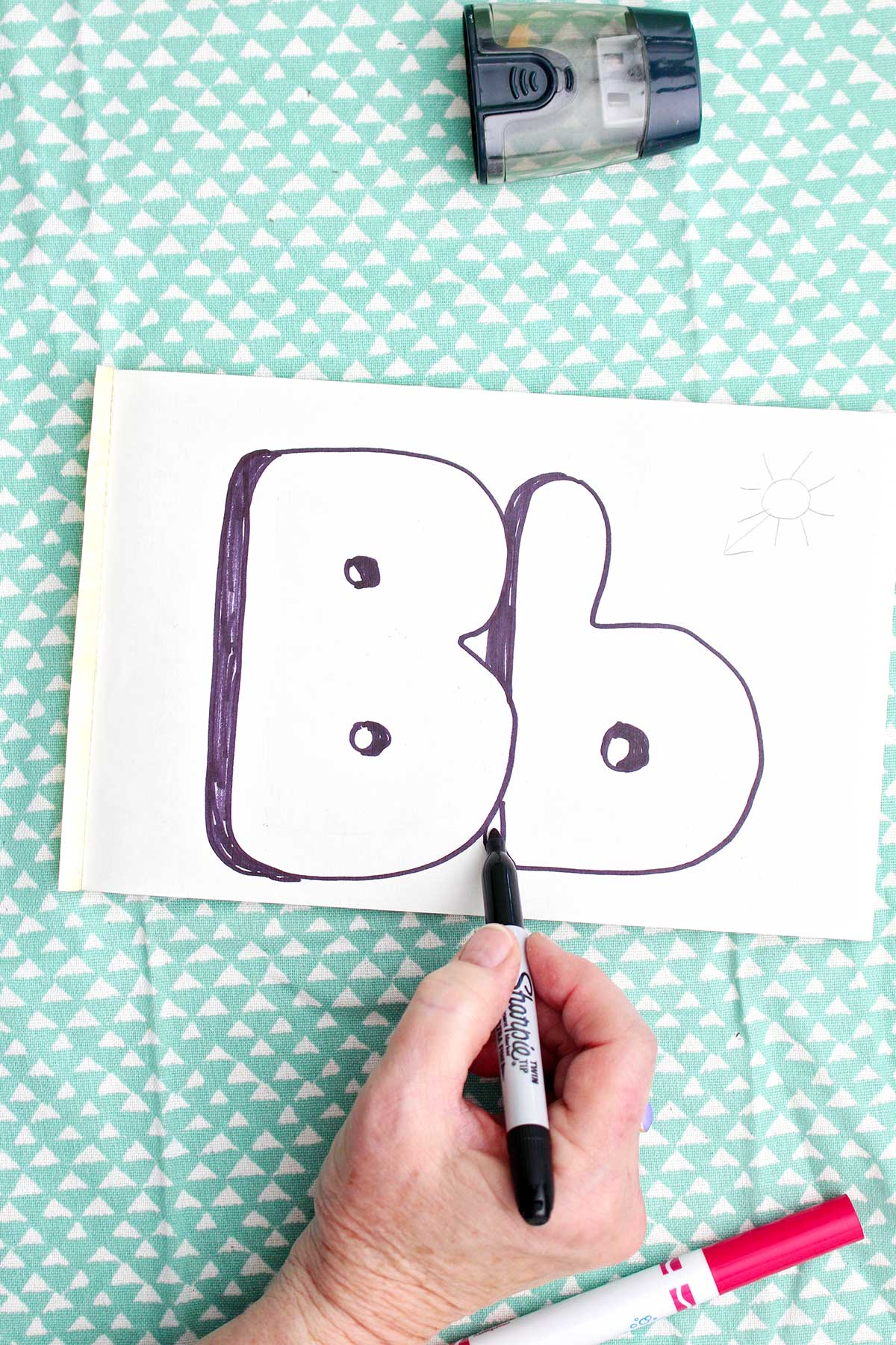 A person using a sharpie marker to add shadow to the upper and lowercase "b".