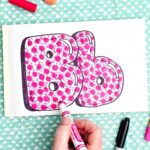 A person coloring in finishing details on the pink pattern inside the "b" bubble letters.