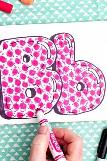 A person coloring in finishing details on the pink pattern inside the "b" bubble letters.
