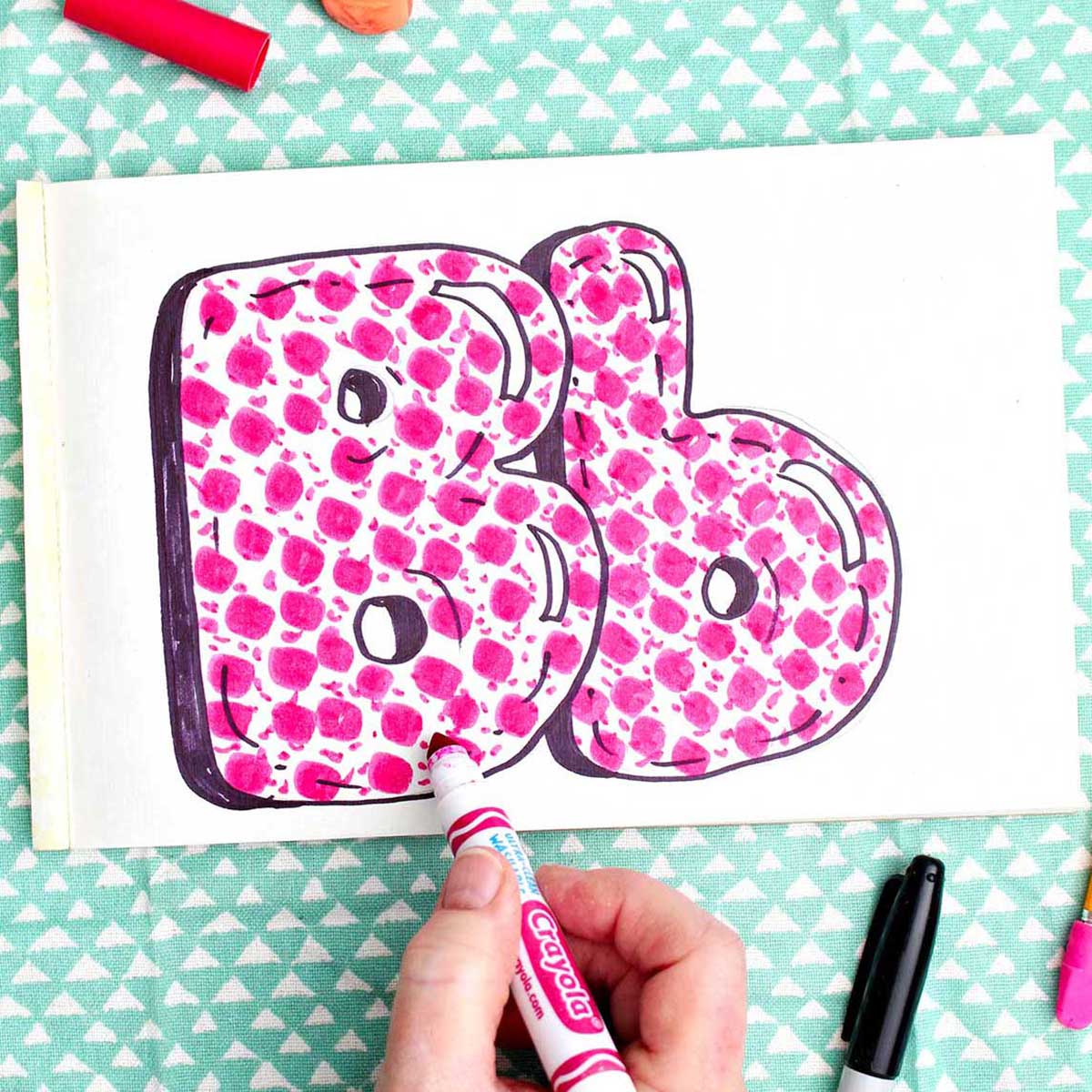 A person coloring in finishing details on the pink pattern inside the "b" bubble letters.