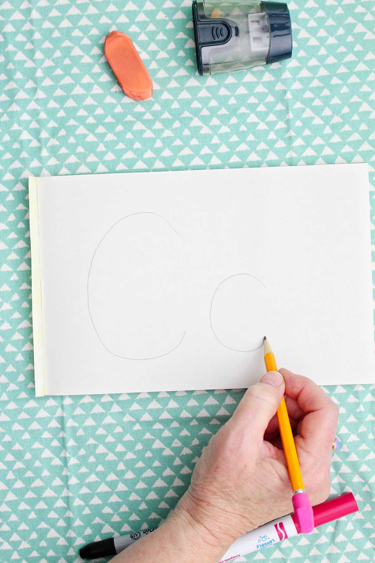 A person writing an upper and lowercase "c" with pencil.