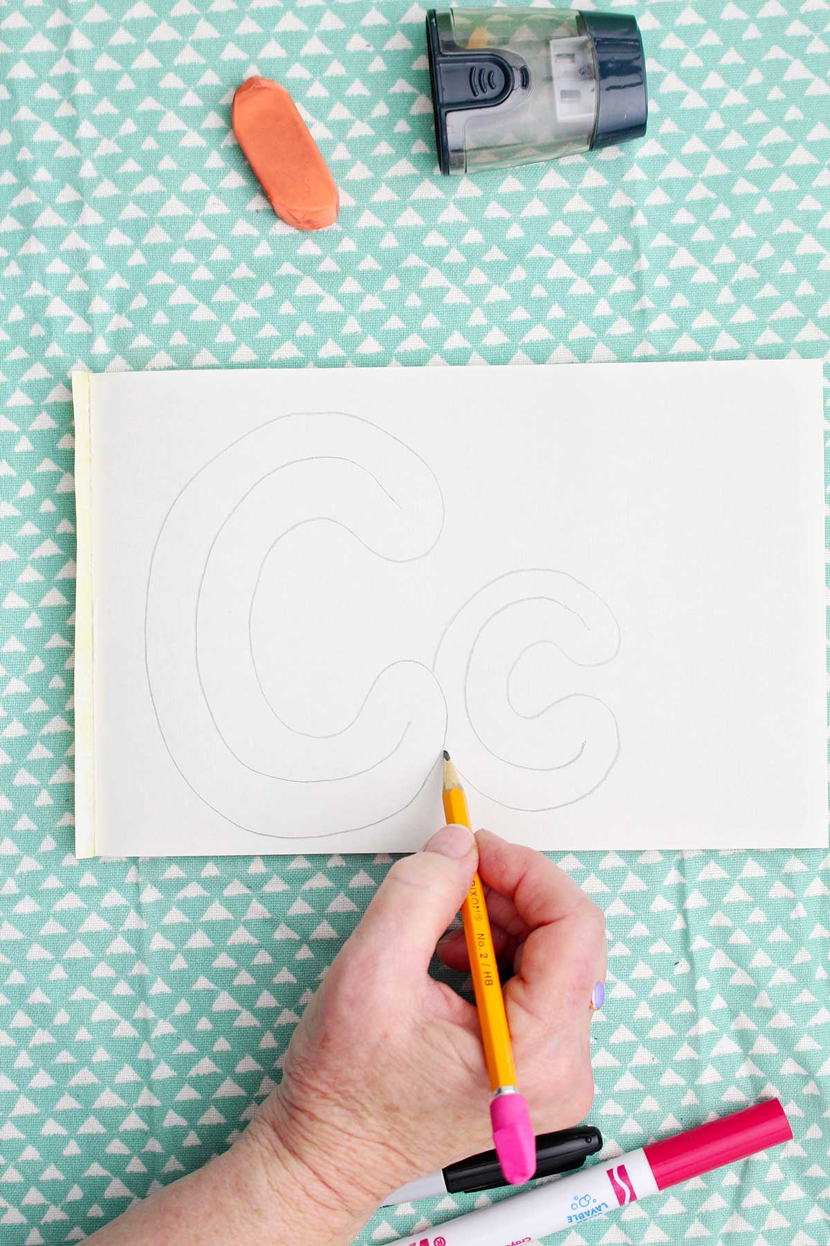 A person sketching a light pencil bubble letter around the pencil drawn "c".