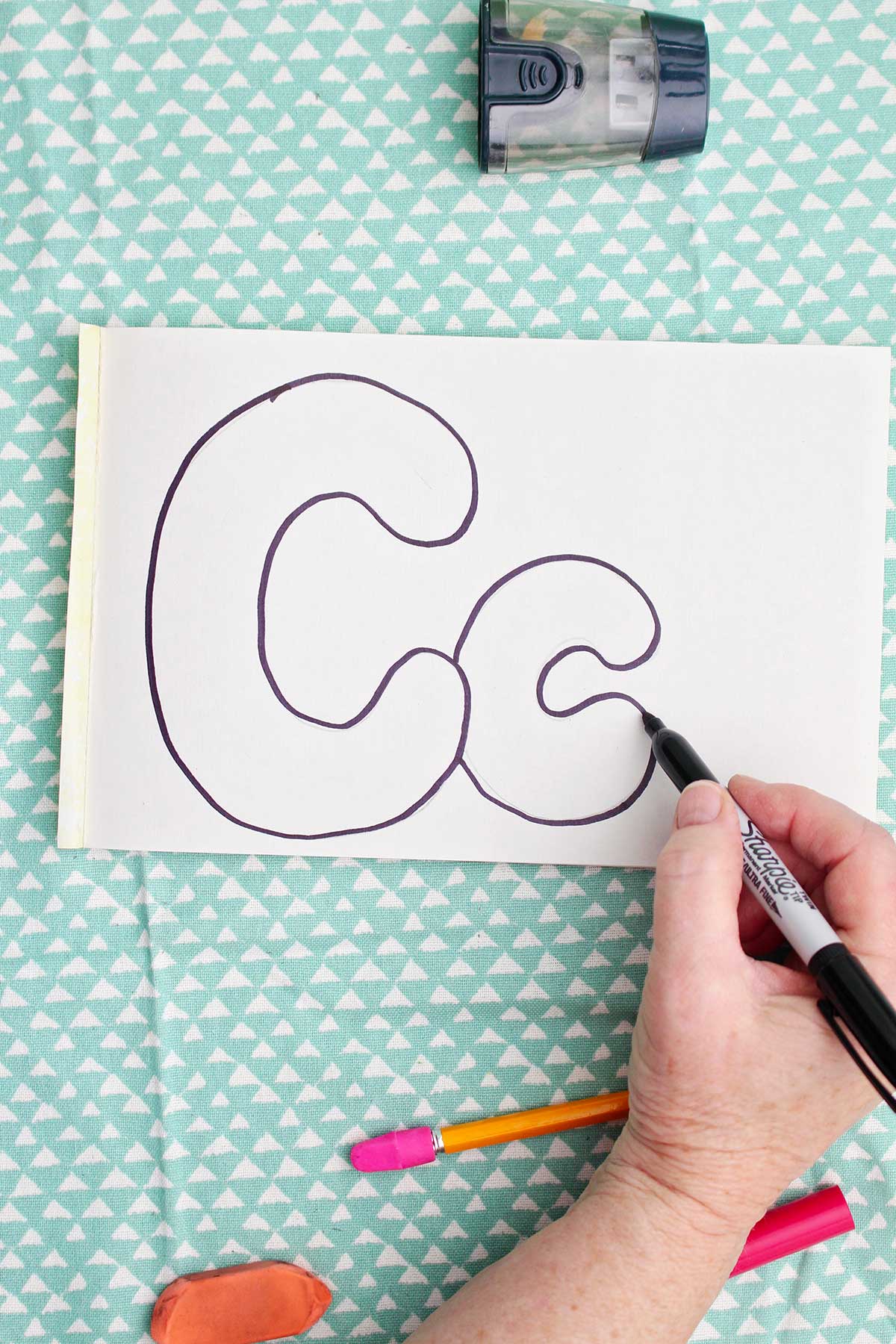 A person outlining with sharpie bubble letters around the pencil drawn "c".