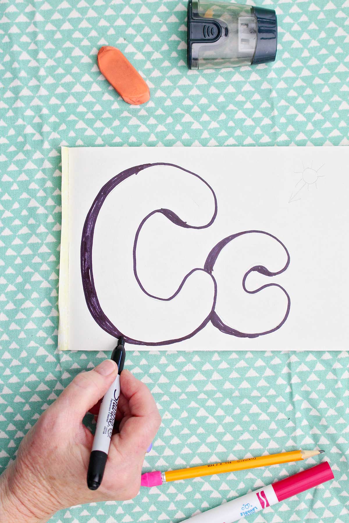 A person using a sharpie marker to add shadow to the upper and lowercase "c".