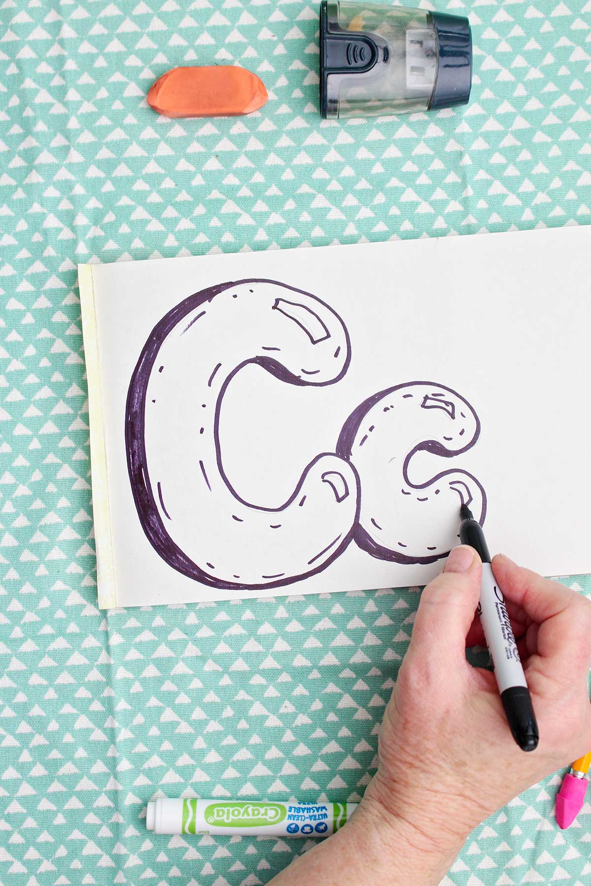 A person adding detail to a lowercase bubble letter "c" with a sharpie marker.