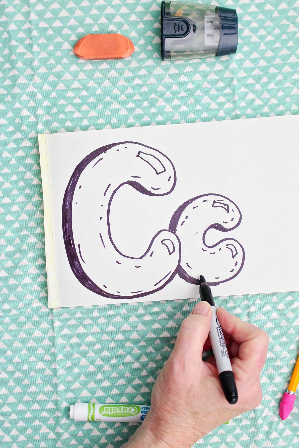 A person adding detail to a lowercase bubble letter "c" with a sharpie marker.
