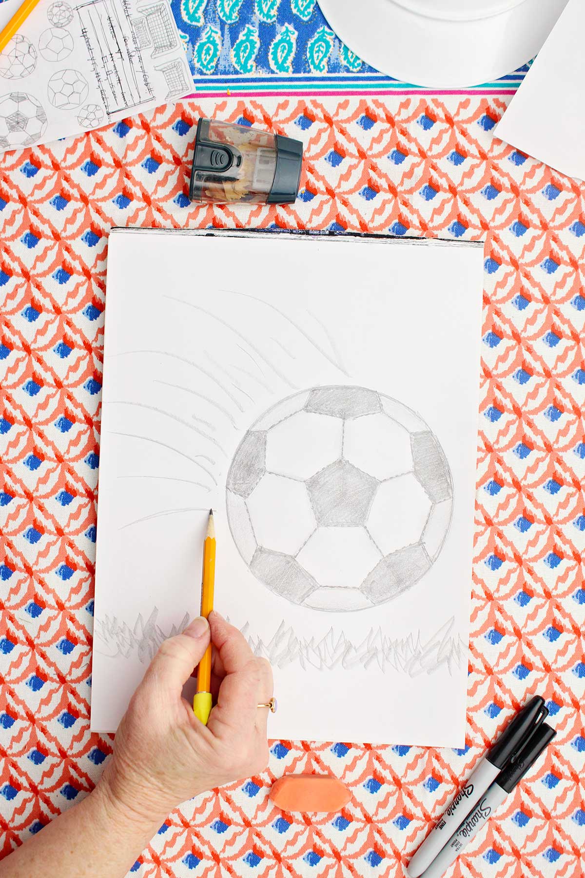 A person adding detail to a pencil sketch of a soccer ball.