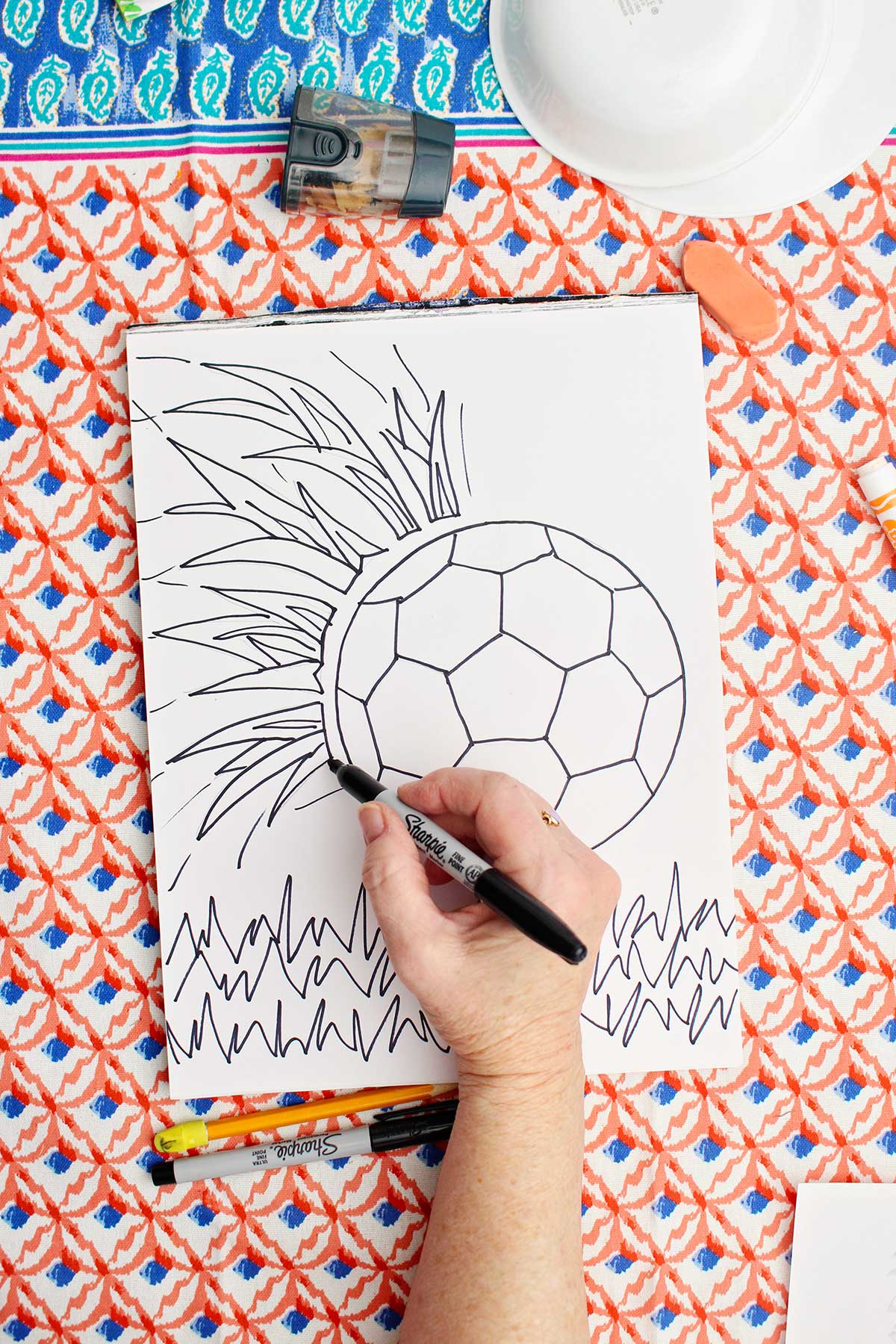 A person going over the pencil sketch of a soccer ball with a sharpie marker.