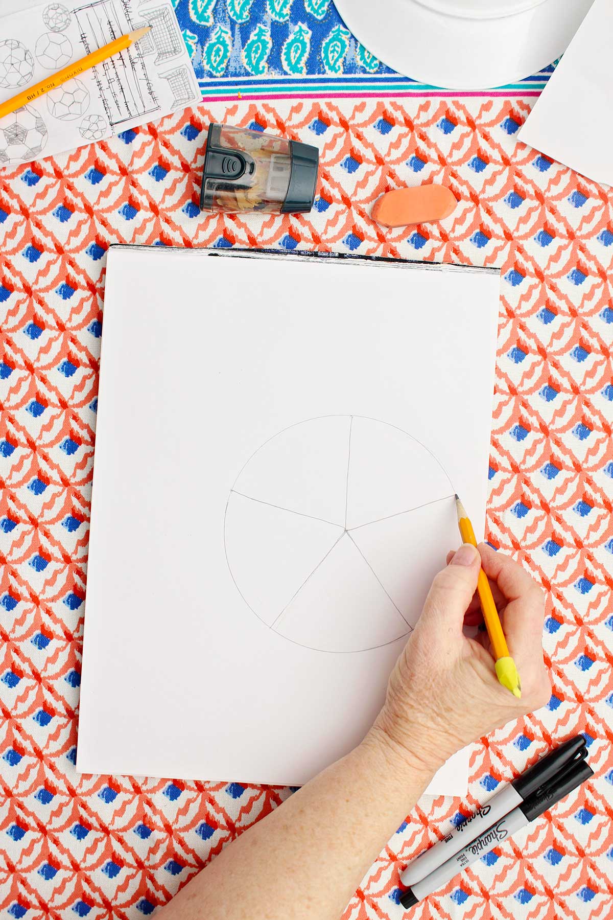 A person dividing a drawing of a circle into 5 equal wedges.