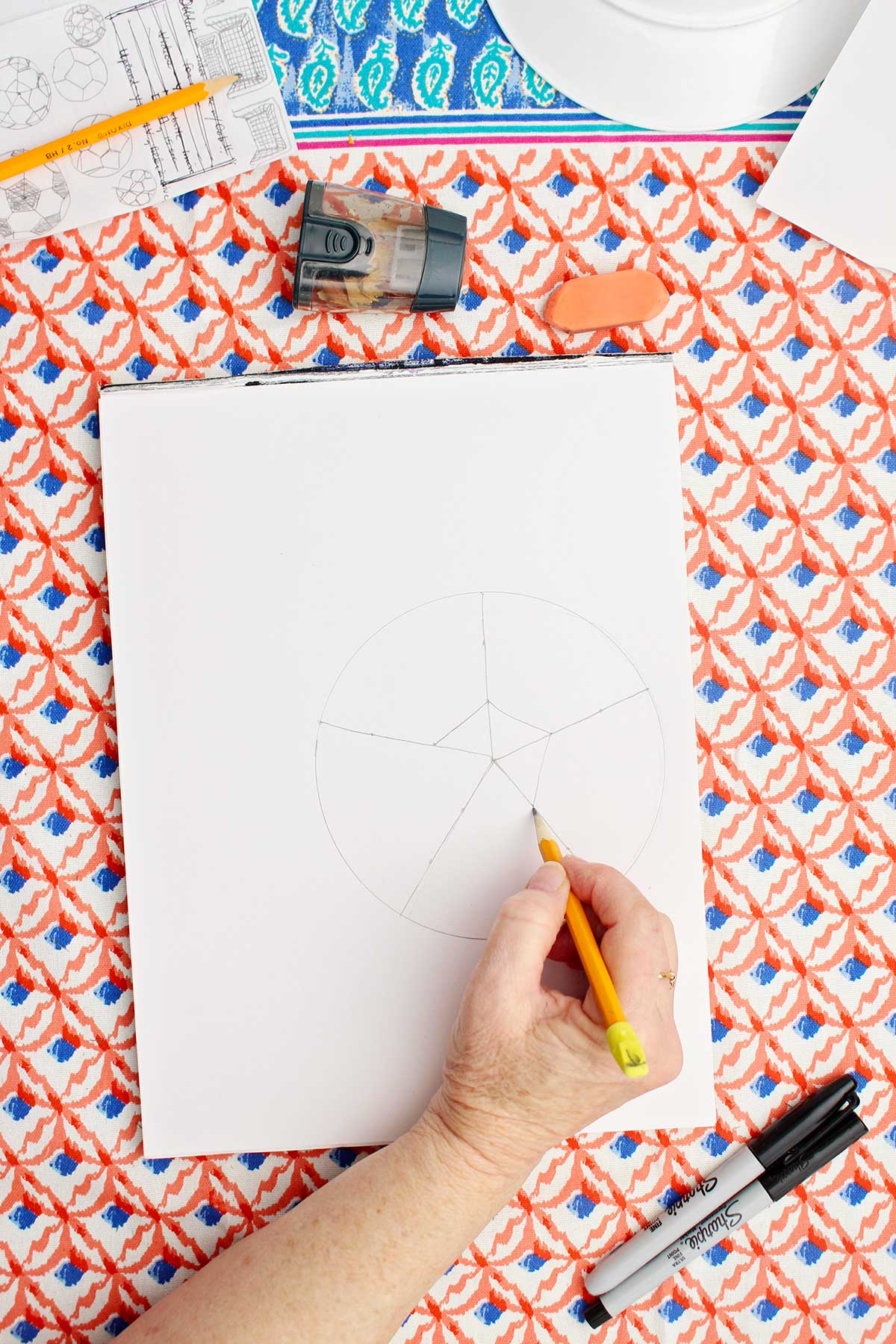 A person drawing the inner shape on the circle that will become a drawing of a soccer ball.