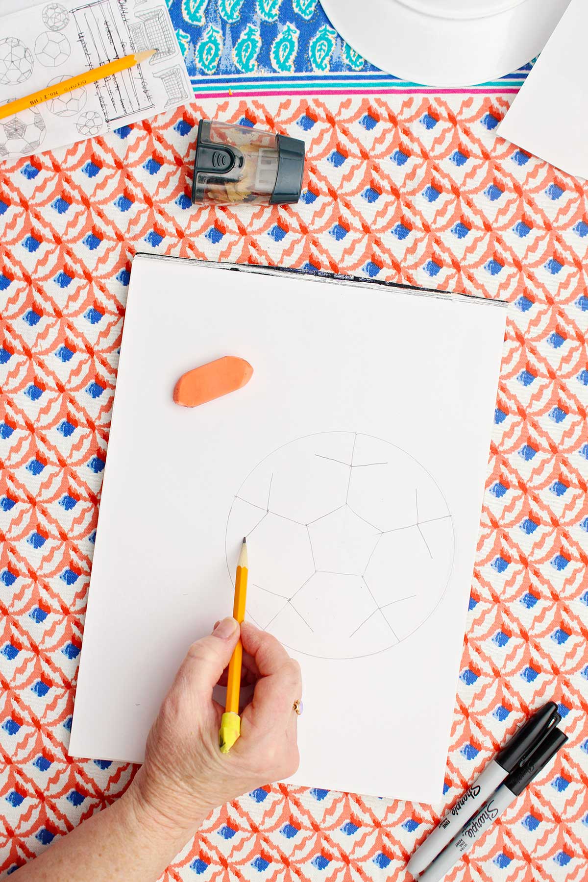 A person drawing a pencil sketch of the pattern of the patches in a soccer ball.