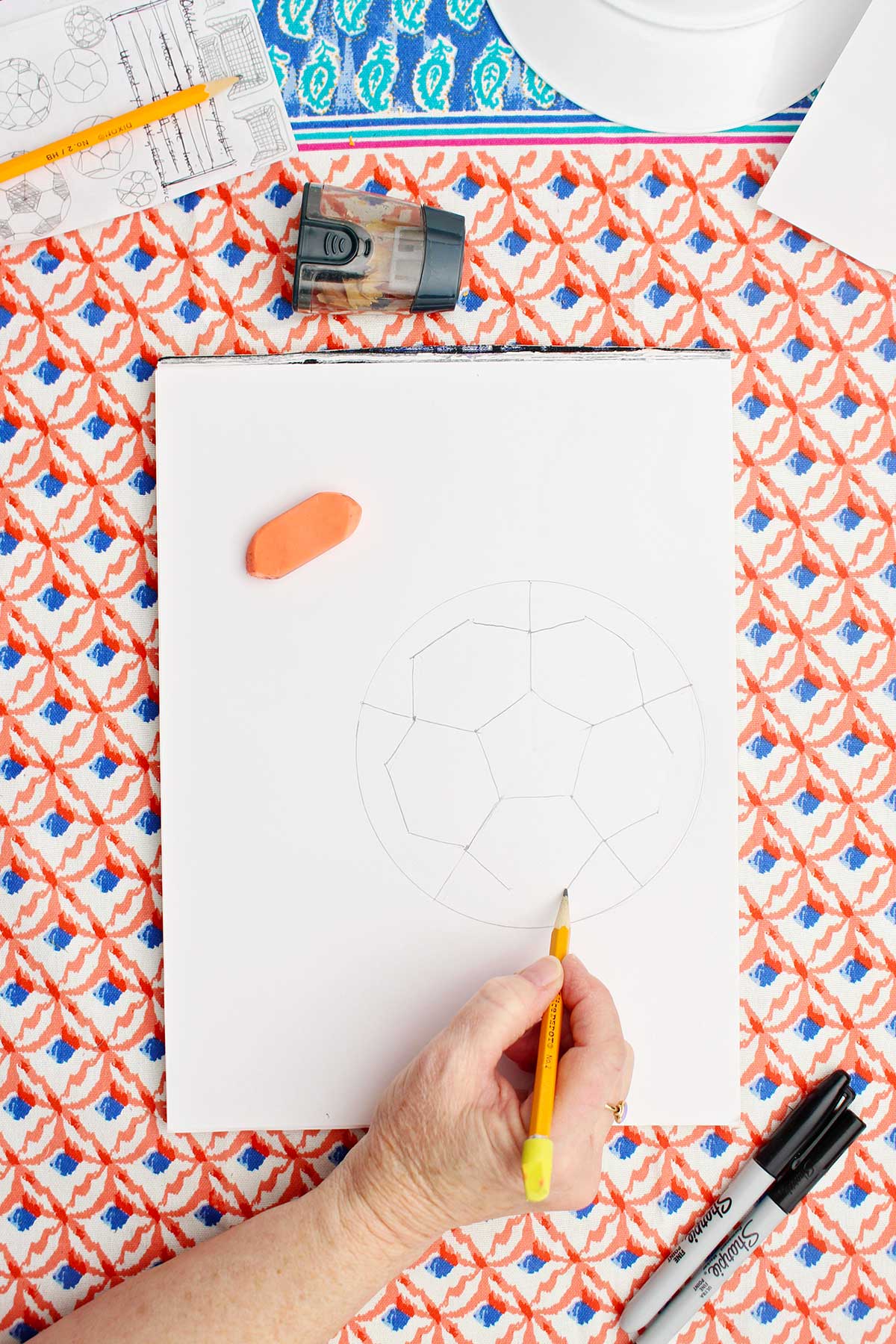 A person drawing a pencil sketch of the pattern of the patches in a soccer ball.