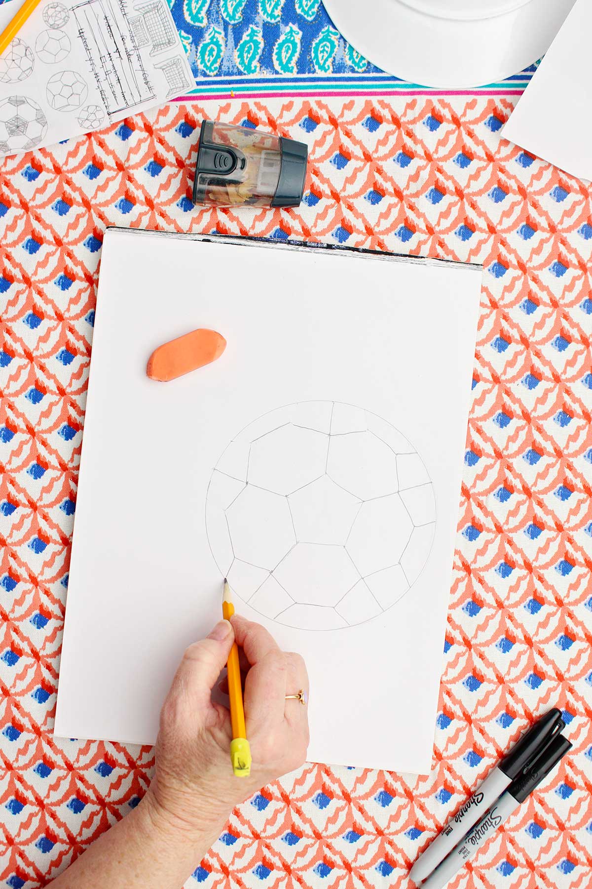 A person drawing a pencil sketch of the pattern of the patches in a soccer ball.
