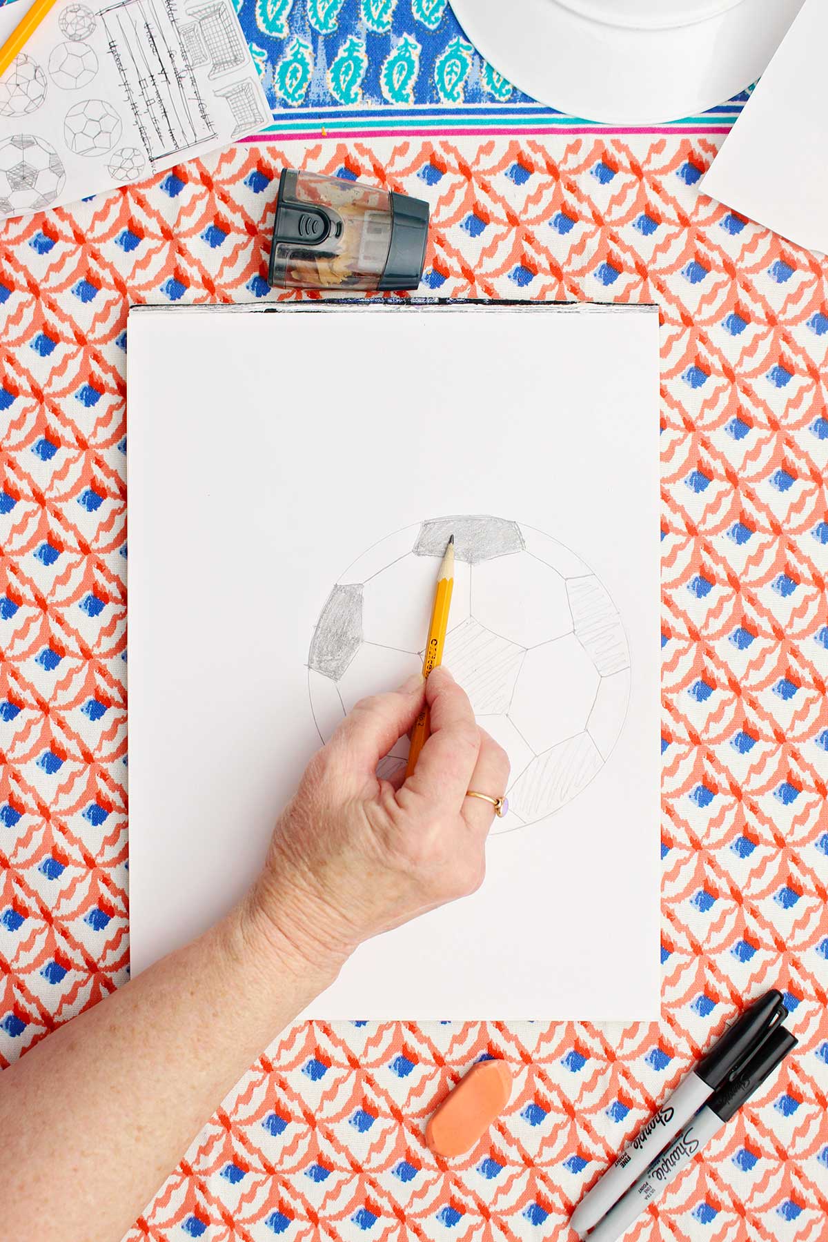 A person shading in the black patches on a soccer ball with pencil.