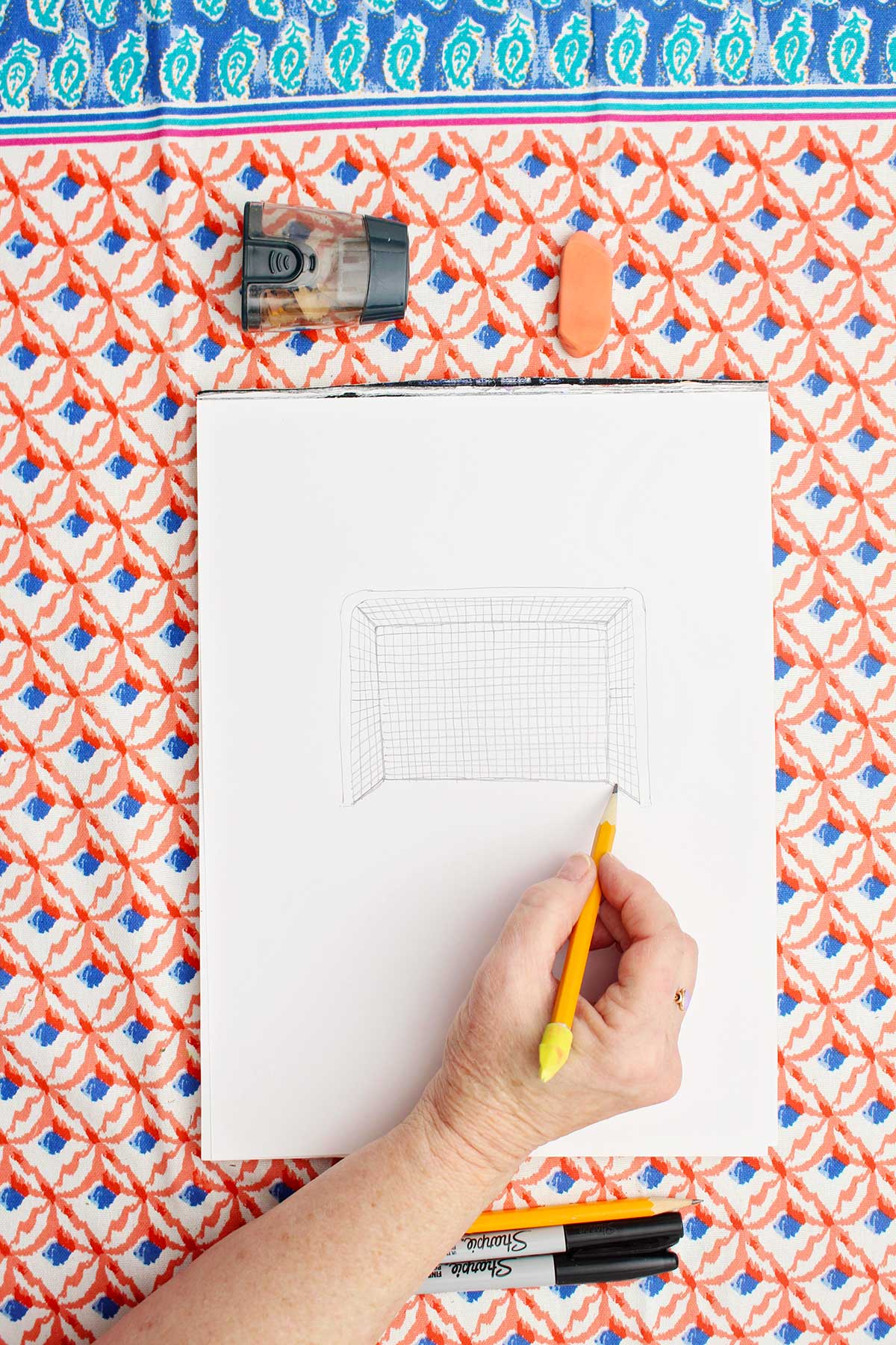 Person sketching a picture of a soccer goal with pencil.