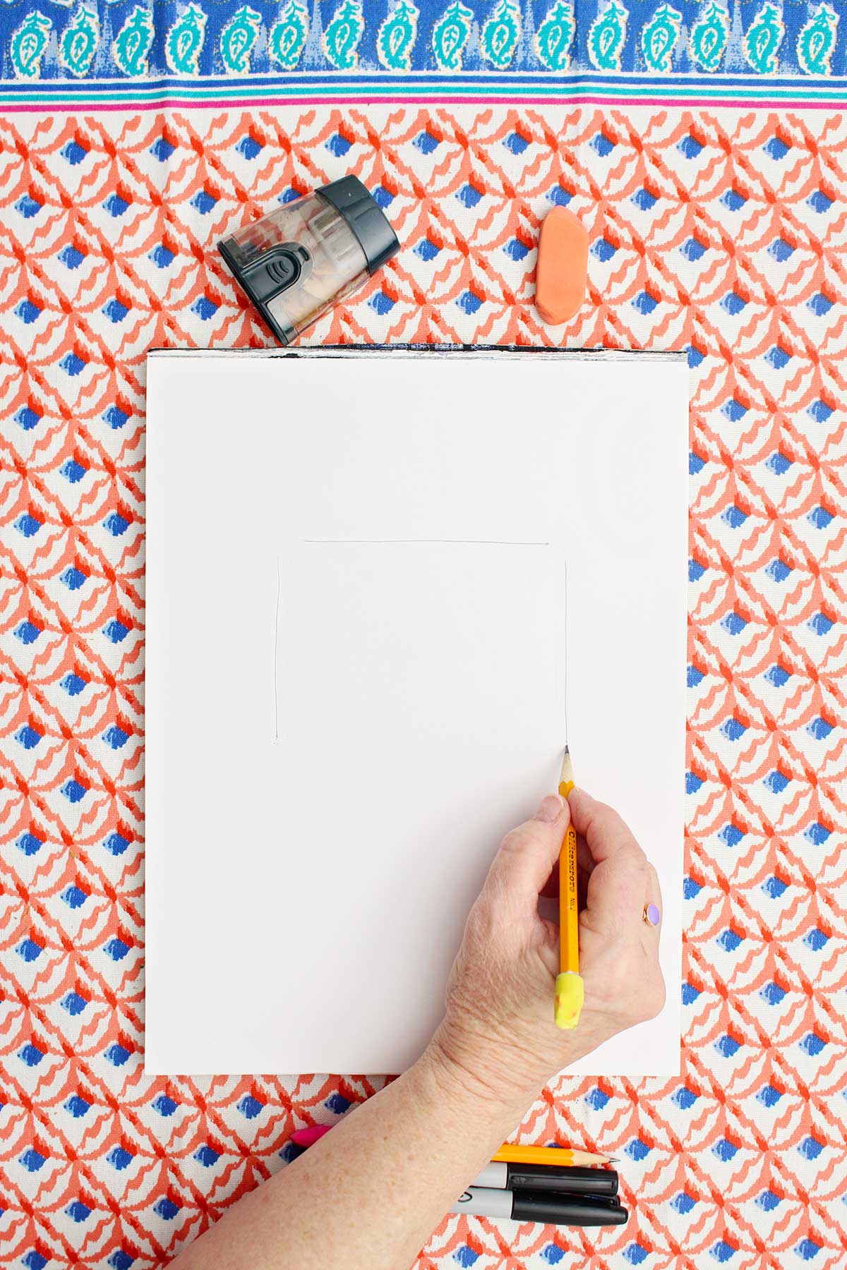 Person drawing three sides of a rectangle in pencil.