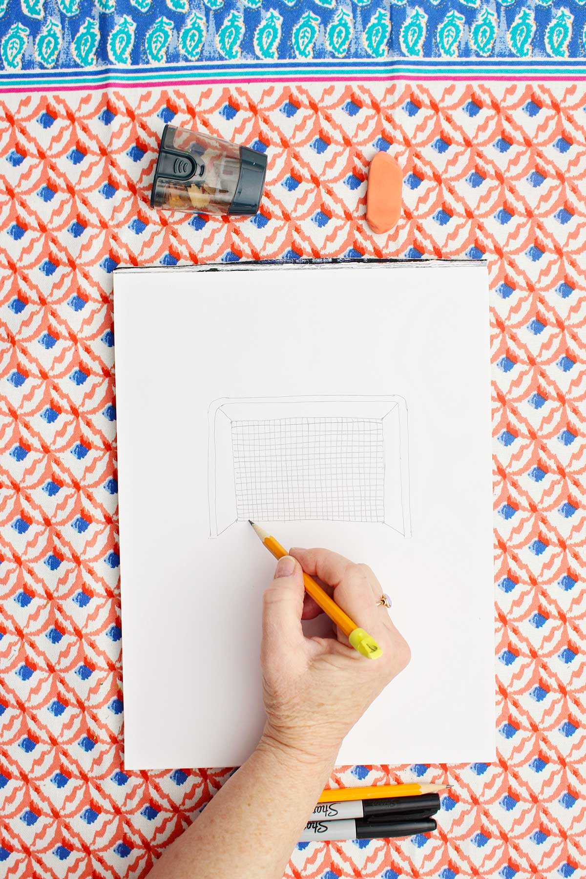 Person sketching a picture of a soccer goal with pencil.