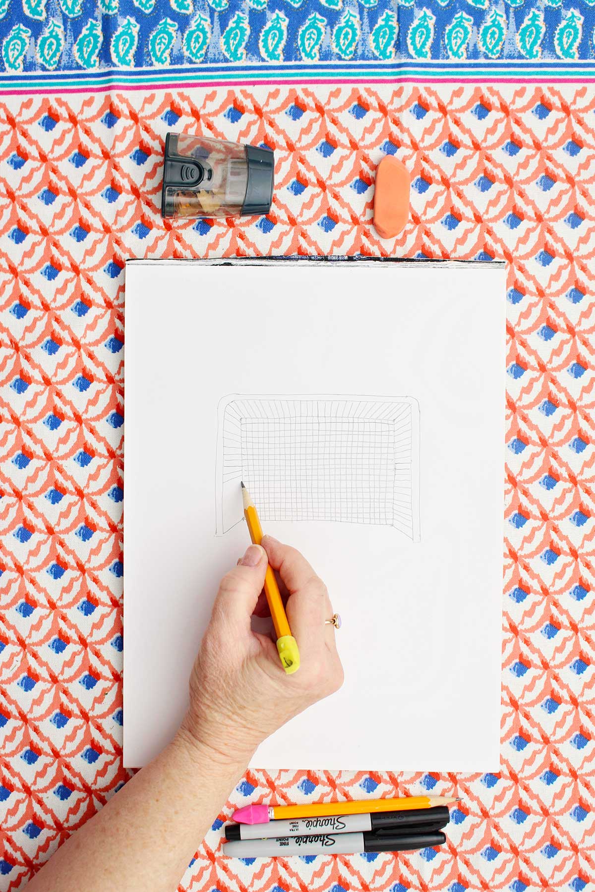 Person sketching a picture of a soccer goal with pencil.