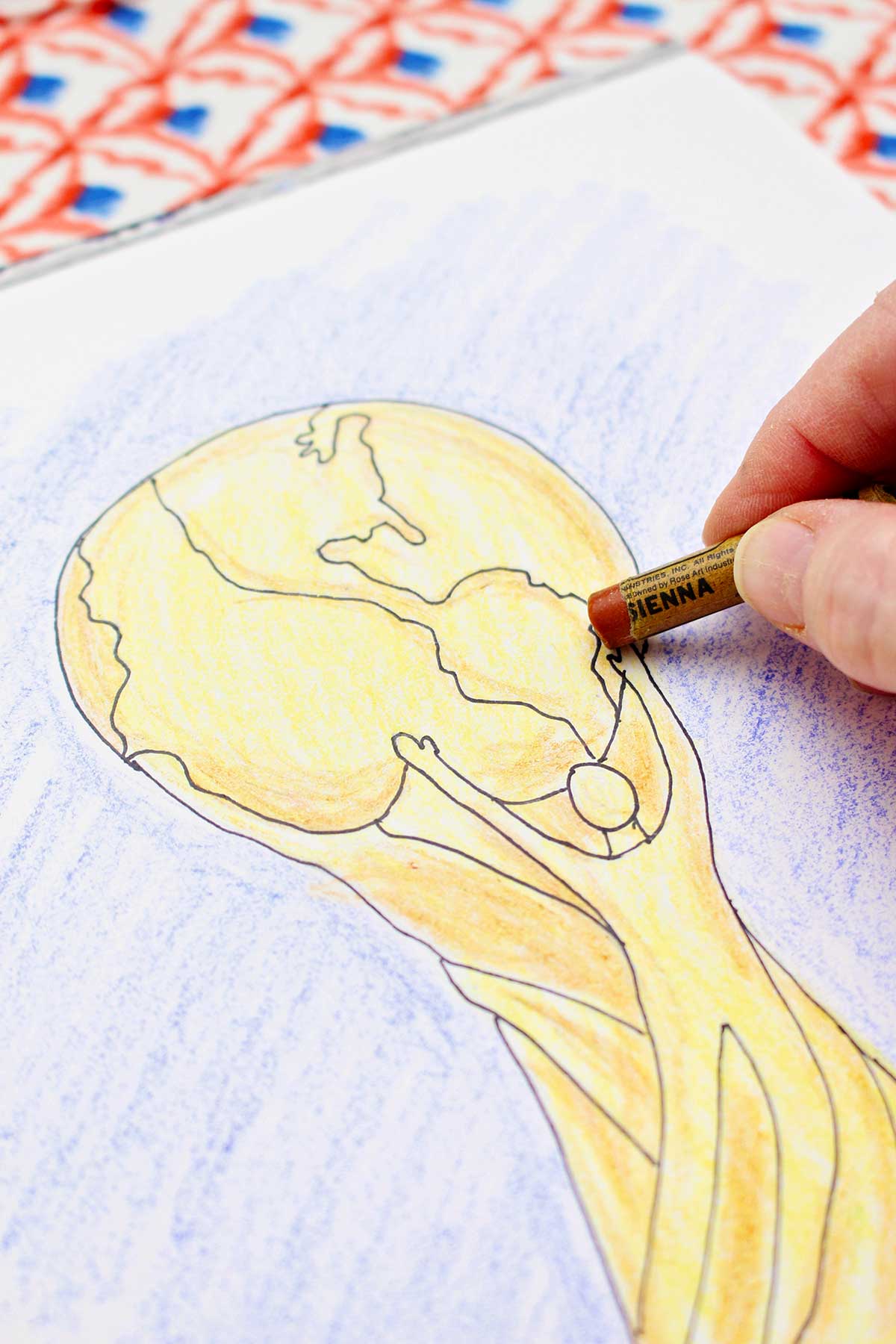 A person adding the finishing touches with a crayon to the FIFA World Cup trophy drawing.