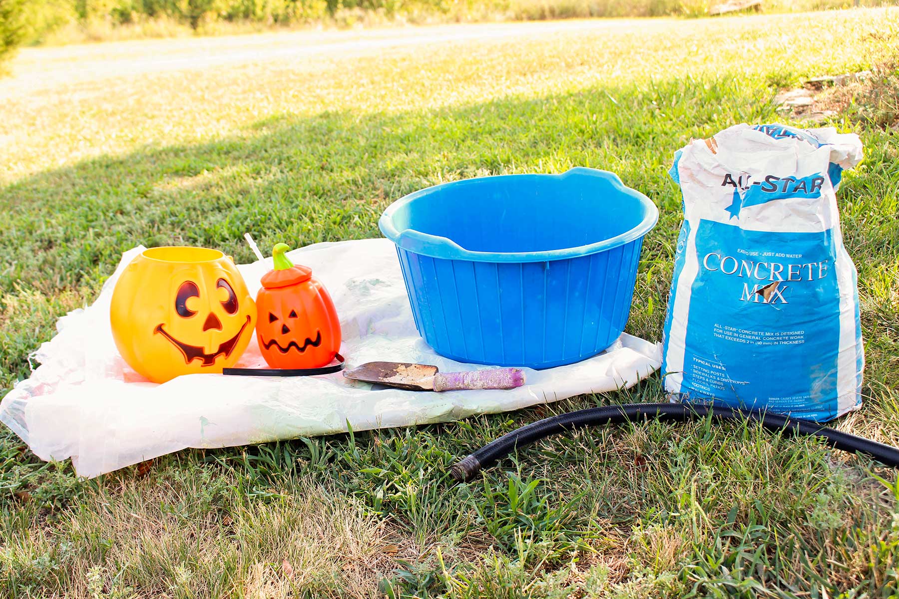 Two plastic pumpkins, a blue tub, and a bag of concrete mix sitting outside in a yard