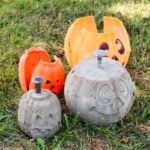 Finished DIY concrete pumpkins sitting next to their plastic shells on the grass.