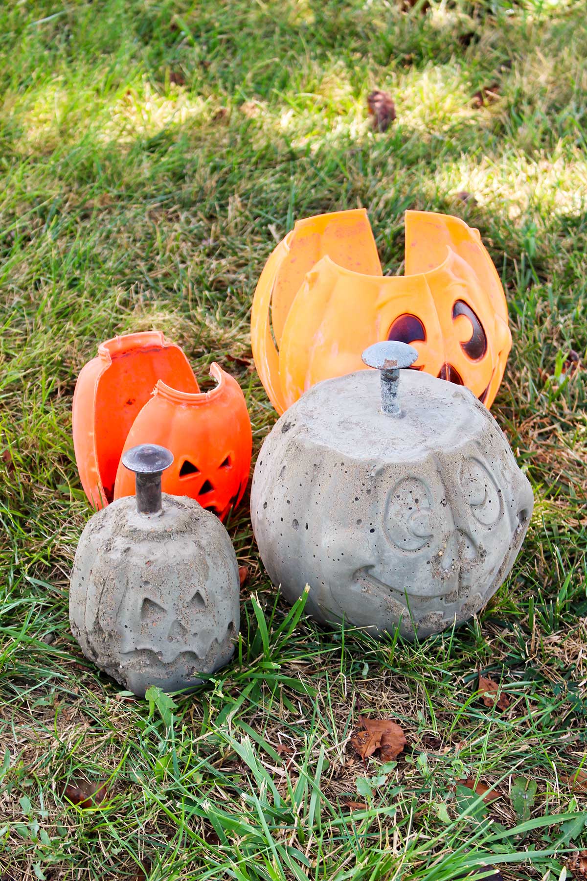 Finished DIY concrete pumpkins sitting next to their plastic shells on the grass.