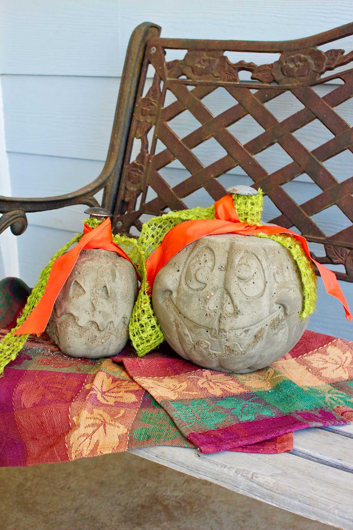 Two concrete pumpkins with green and orange ribbons sitting on a porch