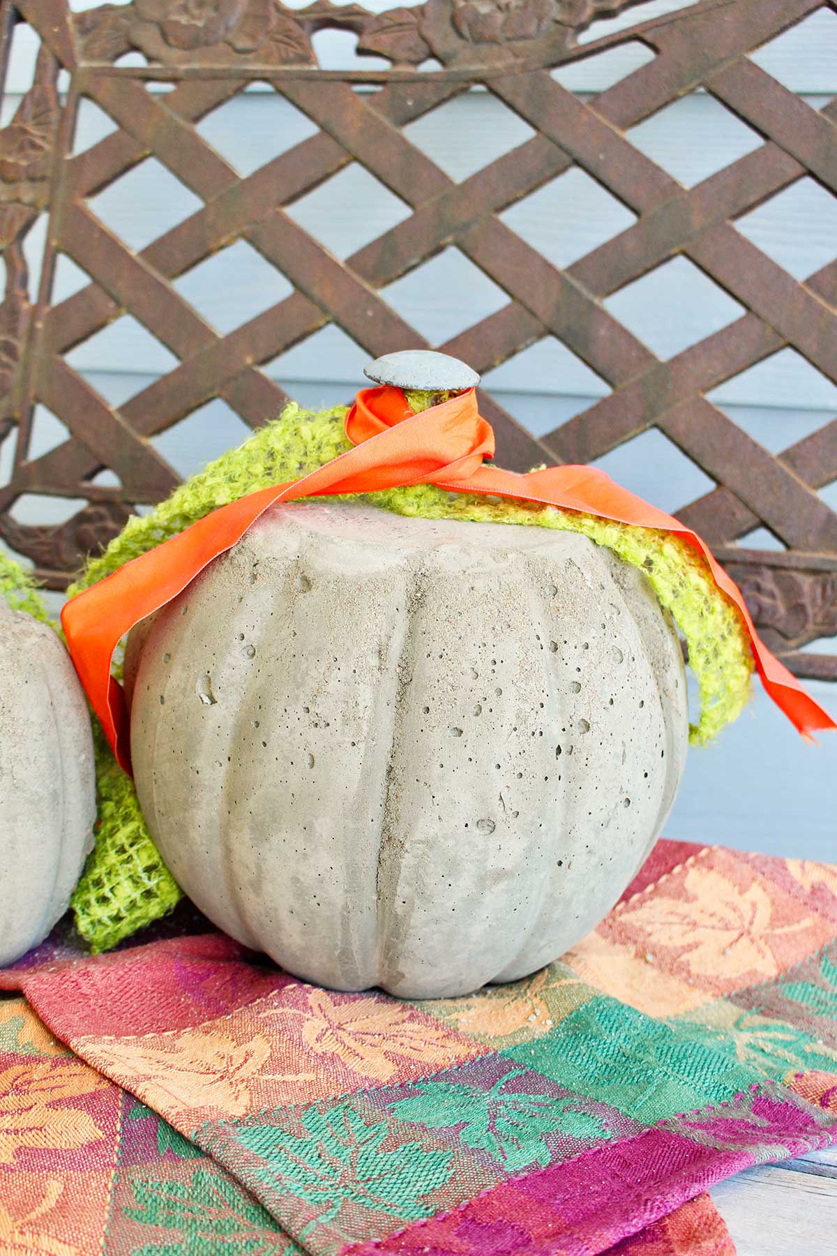 A concrete pumpkin with green and orange ribbons sitting on a porch