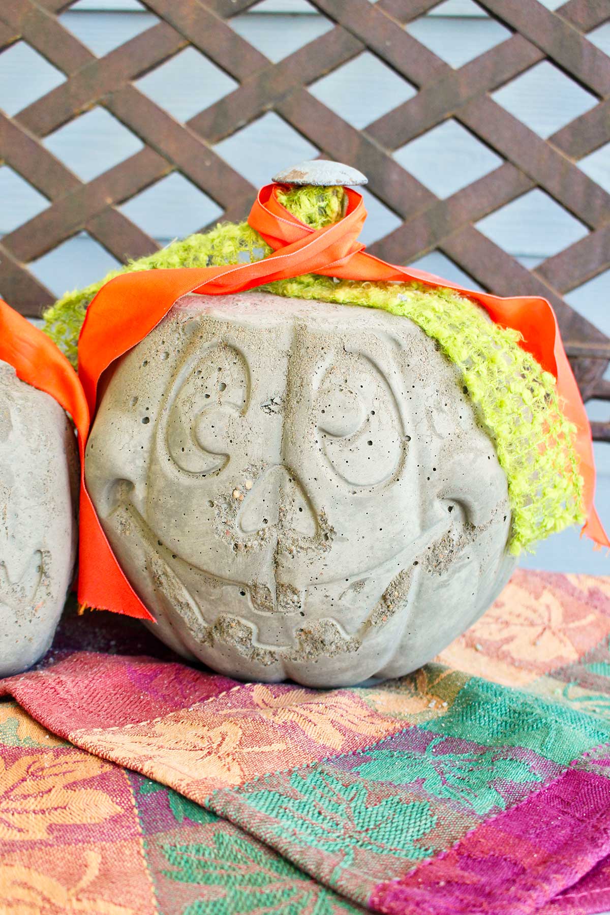 A jack-o-lantern concrete pumpkin with green and orange ribbons sitting on a porch