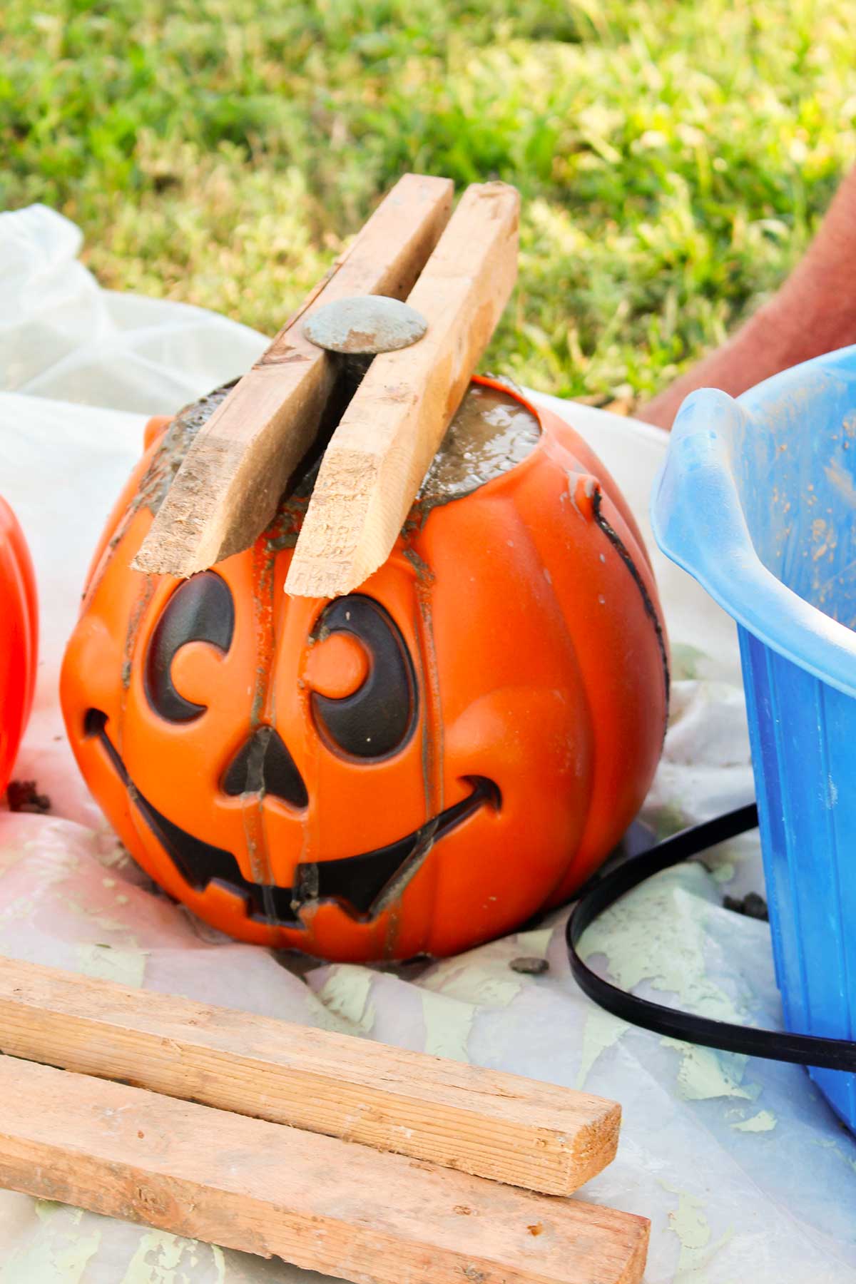 A plastic pumpkin filled with concrete, with wood pieces holding a metal stem in place