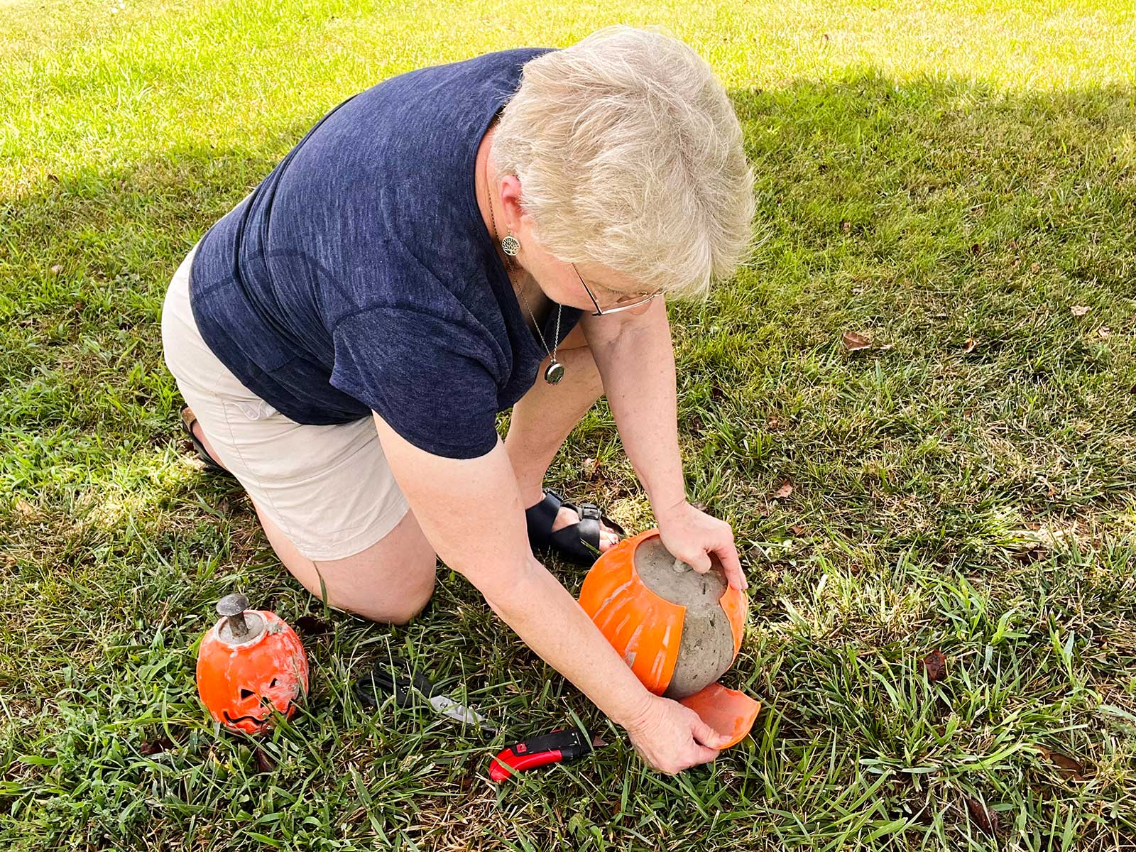 A woman pulling the plastic off a concrete pumpkin in the grass