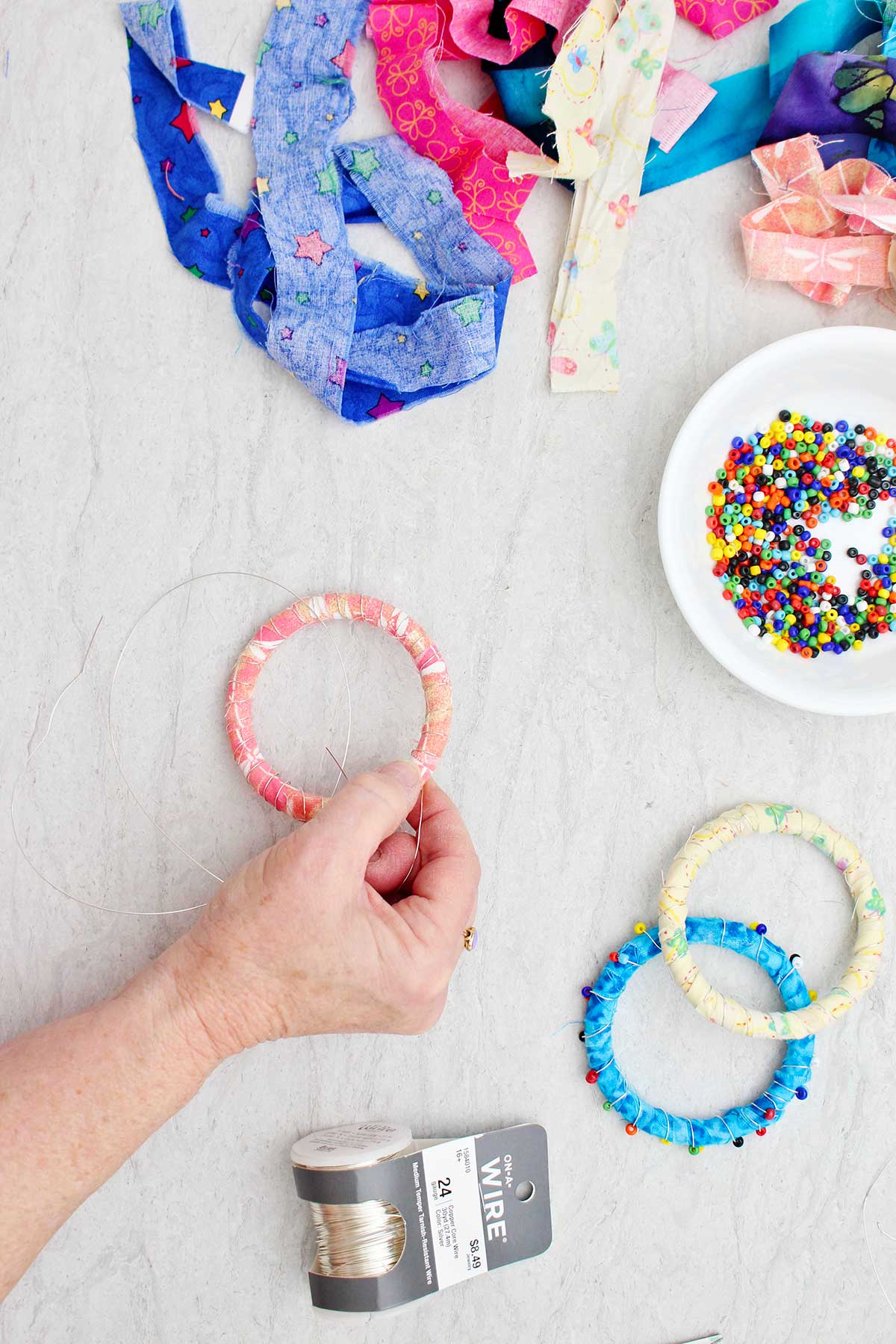 A person wrapping wire around a peach and pink fabric wrapped bracelet.