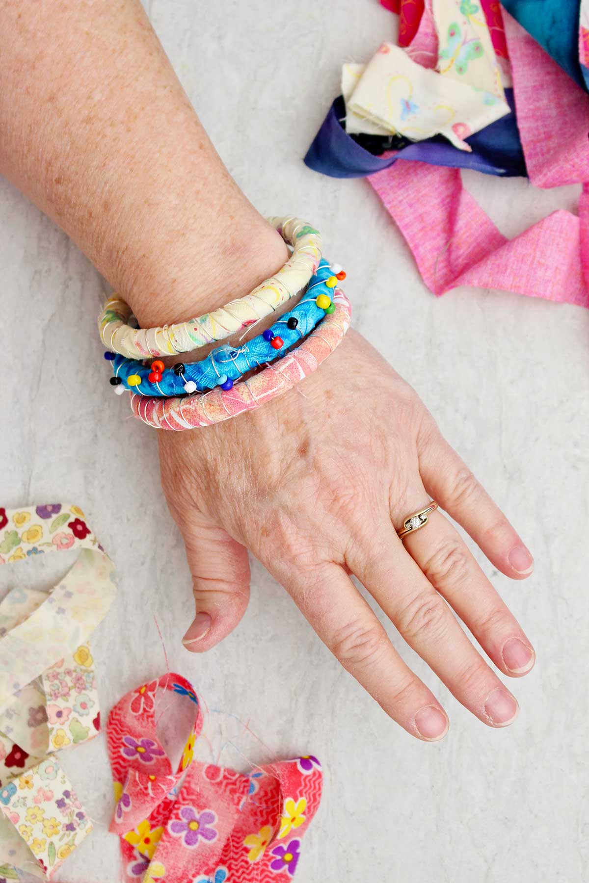 A person wearing three fabric wrapped BoHo bracelets with other scraps of colorful fabric near by.
